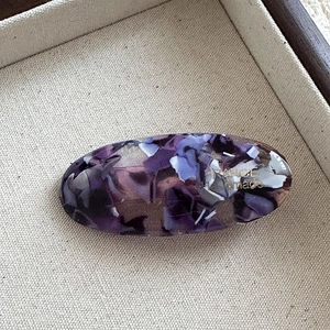 Detail view of oval acetate hair clip with purple marble texture and golden handmade label