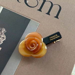 Detail of amber acetate rose hair clip with France Handmade text on brown background