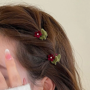 Red flocked flower hair clip with pearl center and green leaf detail on brown hair