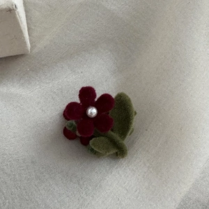 Close-up of a handmade burgundy flocked flower hair clip with pearl and green leaves