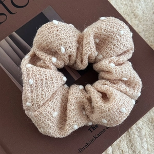 Dettaglio dell'elastico in maglia beige con pompon bianchi su un libro