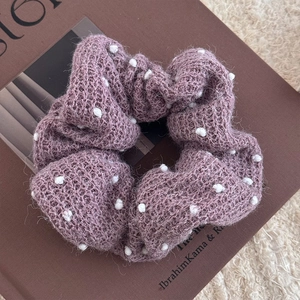 Dettaglio di uno scrunchie in maglia grigio-viola spesso con pompon bianchi 3D