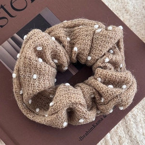 Dettaglio dell'elastico in maglia kaki con pompon bianchi su tessuto di lana