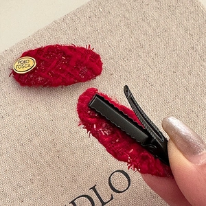 Detail of red tweed hair clip with gold logo plate and metal duckbill clip back