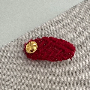 Macro view of a red tweed hair clip with a vintage gold metal emblem on linen fabric