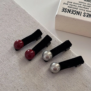Close-up of four velvet hair clips with red and silver beads on a beige texture