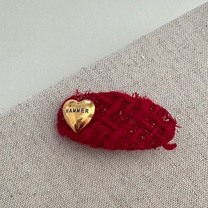 Detailed macro view of red tweed fabric hair clip with a gold heart hammer emblem