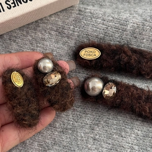 Detail view of brown fuzzy hair clip with golden plaque, faux pearl and amber crystal