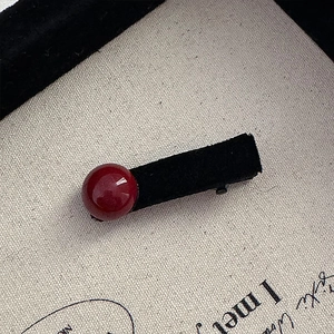 Detailed macro view of a vintage red bead duckbill hair clip with black velvet fabric wrapping