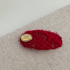 Close-up of a red tweed heart-shaped hair clip featuring an oval gold POKO FOSCA metal logo