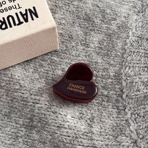 Dettaglio della pinza per capelli a cuore in acetato marrone con logo dorato inciso