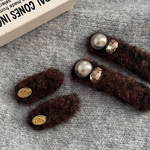 Close-up of four brown faux fur hair clips with pearls, rhinestones and gold brand plates