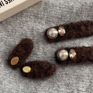 Detailed macro of vintage plush hair clips with gold logo and pearl embellishments