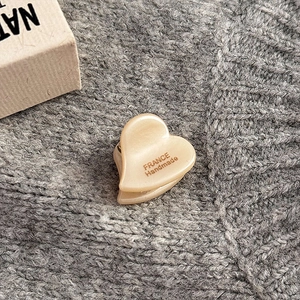 Dettaglio di piccola molletta a cuore in acetato con etichetta dorata su maglia