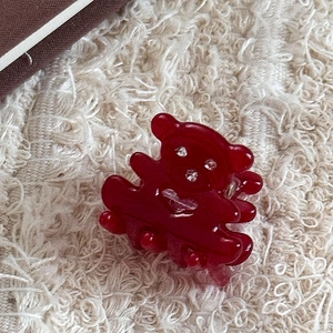 Détail d'une pince à cheveux ours rouge translucide avec strass sur un fond beige doux