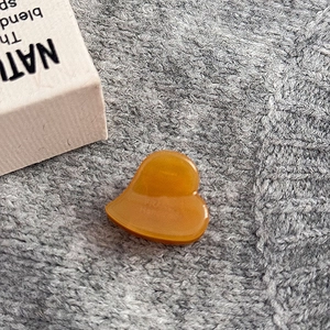 Dettaglio della molletta a cuore in acetato ambrato su sfondo in maglia grigia