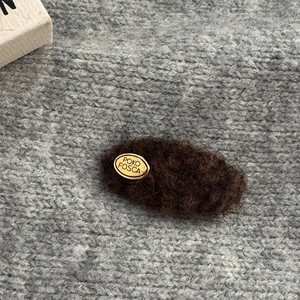 Close-up of fluffy dark brown oval hair clip with gold POKO FOSCA metal logo tag
