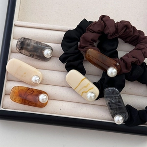 Dettaglio di fermagli per capelli in acetato marmorizzato con perle su vassoio beige