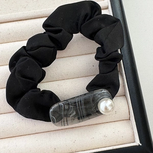 Dettaglio di scrunchie nero con motivo marmoreo e decorazione con perla bianca