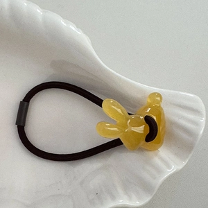 Detail eines gelben Kaninchen-Anhängers aus Harz am elastischen Haargummi in Schale