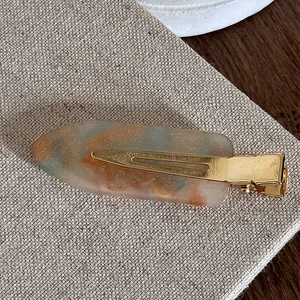Detail of cellulose acetate hair clip with orange and gold marble pattern on linen