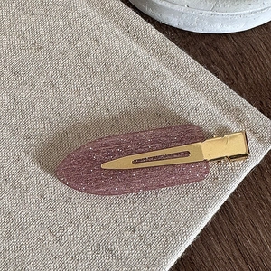 Gros plan d'une barrette à paillettes roses avec base en métal doré sur tissu rustique