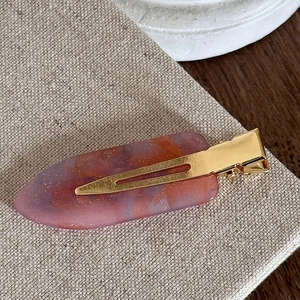 Detail of a marble-textured resin hair clip with gold metal base on linen surface