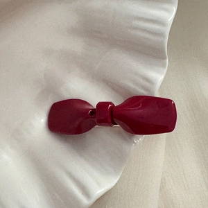 Détail d'une pince à cheveux nœud bordeaux brillant sur une assiette décorative