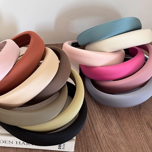 Detail view of colorful matte satin padded headbands stacked on a vintage wooden surface