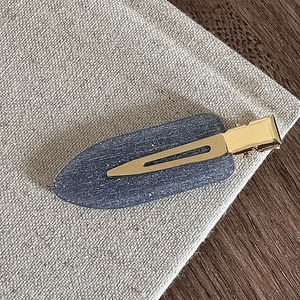 Détail d'une pince à cheveux mate bleue pailletée avec base dorée sur tissu naturel