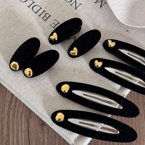 Detail of black flocked BB hair clips with gold heart accents on a rustic fabric background