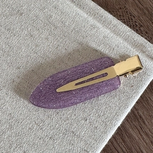 Détail d'une barrette violette scintillante avec clip en métal doré sur tissu en lin texturé