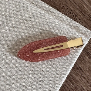 Détail d'une barrette en résine marron rouge avec paillettes fines et base dorée