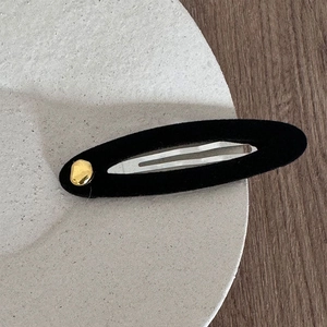 Detail showing the black velvet texture and golden hammered metal accent of the hair clip
