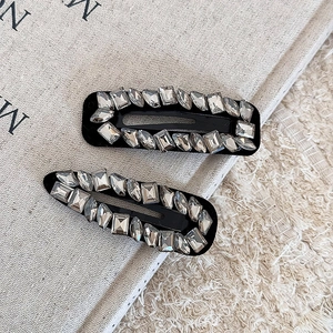 Detail view of two luxury black hair clips with sparkling rhinestones on grey fabric background
