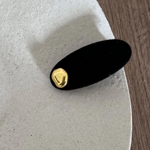 Detailed close-up of a minimalist black velvet hair clip with a stylish gold metallic accent