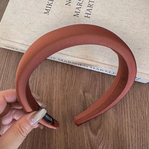 Detail of caramel brown padded satin headband featuring a black woven brand label on wood