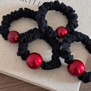 Close-up of black scrunchies with large glossy red beads on a minimalist display