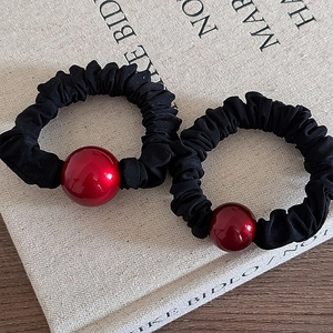 Close-up of red bead and black pleated fabric scrunchies on a decorative book background