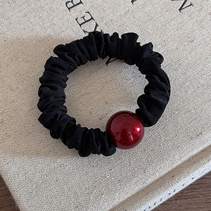 Detailed view of a black pleated elastic hair scrunchie with a glossy wine red bead accent