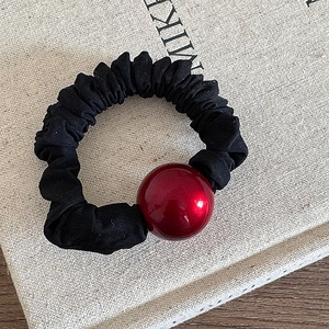 Detail showing a black elastic scrunchie with a large glossy red decorative ball bead