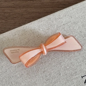 Détail d'une barrette nœud en acétate rose translucide avec logo doré de qualité