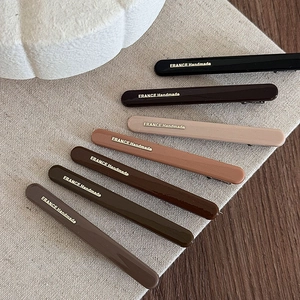 Detailed macro view of seven glossy retro-colored duckbill hair clips with gold lettering