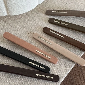 Close-up of handmade acrylic hair clips in earth tones with gold lettering details