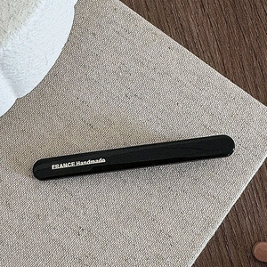 Close-up of black handmade hair clip with France Handmade lettering on fabric background