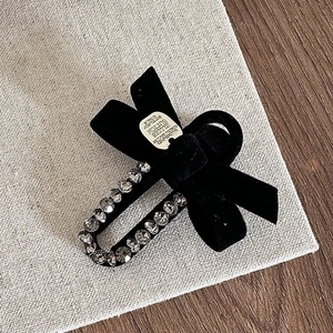 Detail view of black velvet bow hair clip with sparkling rhinestones and metal label