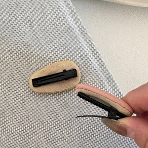 Detail showing the metal duckbill clip with anti-slip teeth and cream leather padding