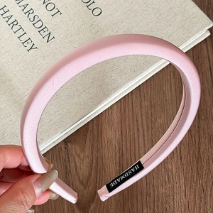 Detailed view of pink satin padded headband with black handmade label on vintage book