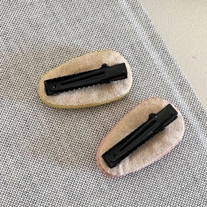 Detail view of two minimalist cream leather hair clips with metal duckbill back structure