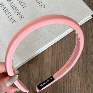 Detail view of pink satin padded headband with a black handmade label on wooden table